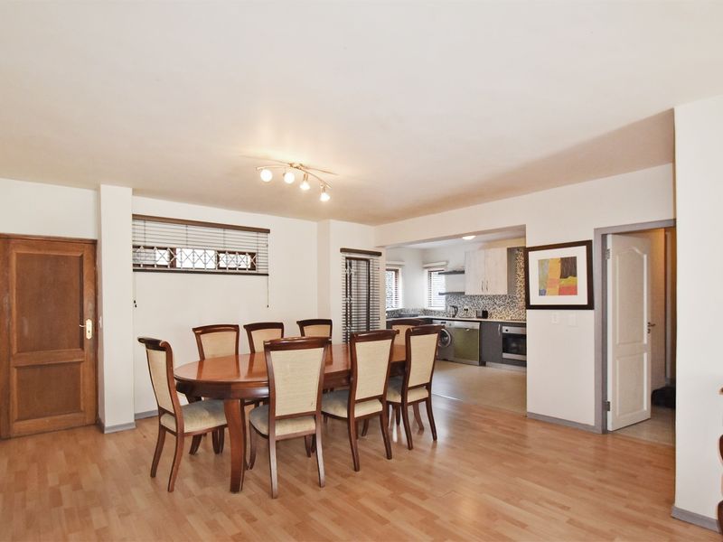Open-plan dining area flowing into a functional kitchen with built-in cabinetry, oven, and extractor fan, featuring laminate flooring throughout.