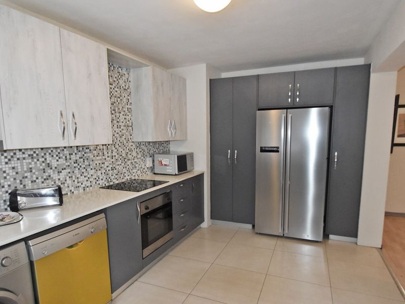 Modern kitchen featuring two-tone cabinetry, mosaic tile backsplash, stone countertops, and integrated appliances including an electric hob and oven.