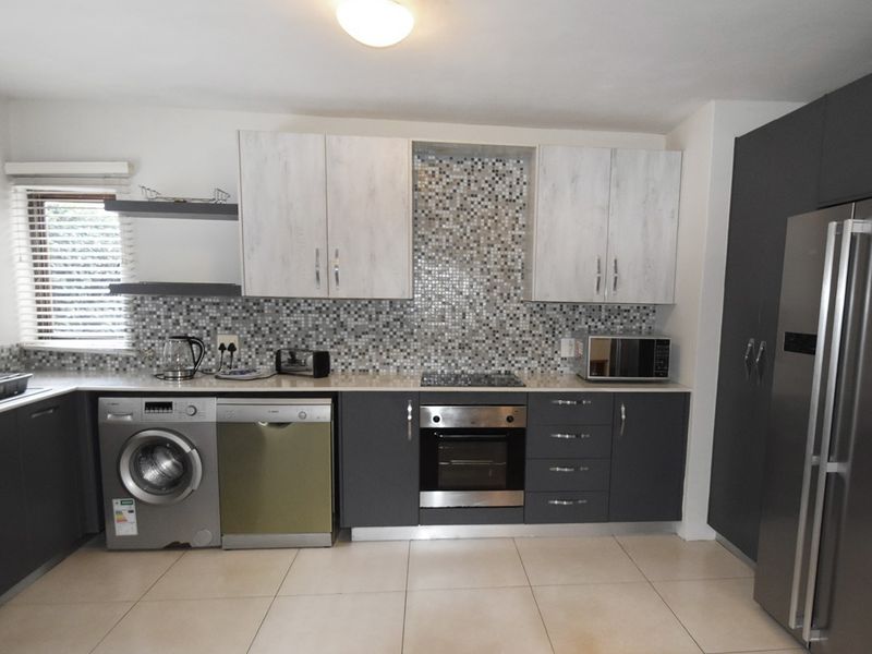Modern kitchen featuring two-tone cabinetry, mosaic tile backsplash, integrated oven, hob, and tiled flooring with ample storage space.