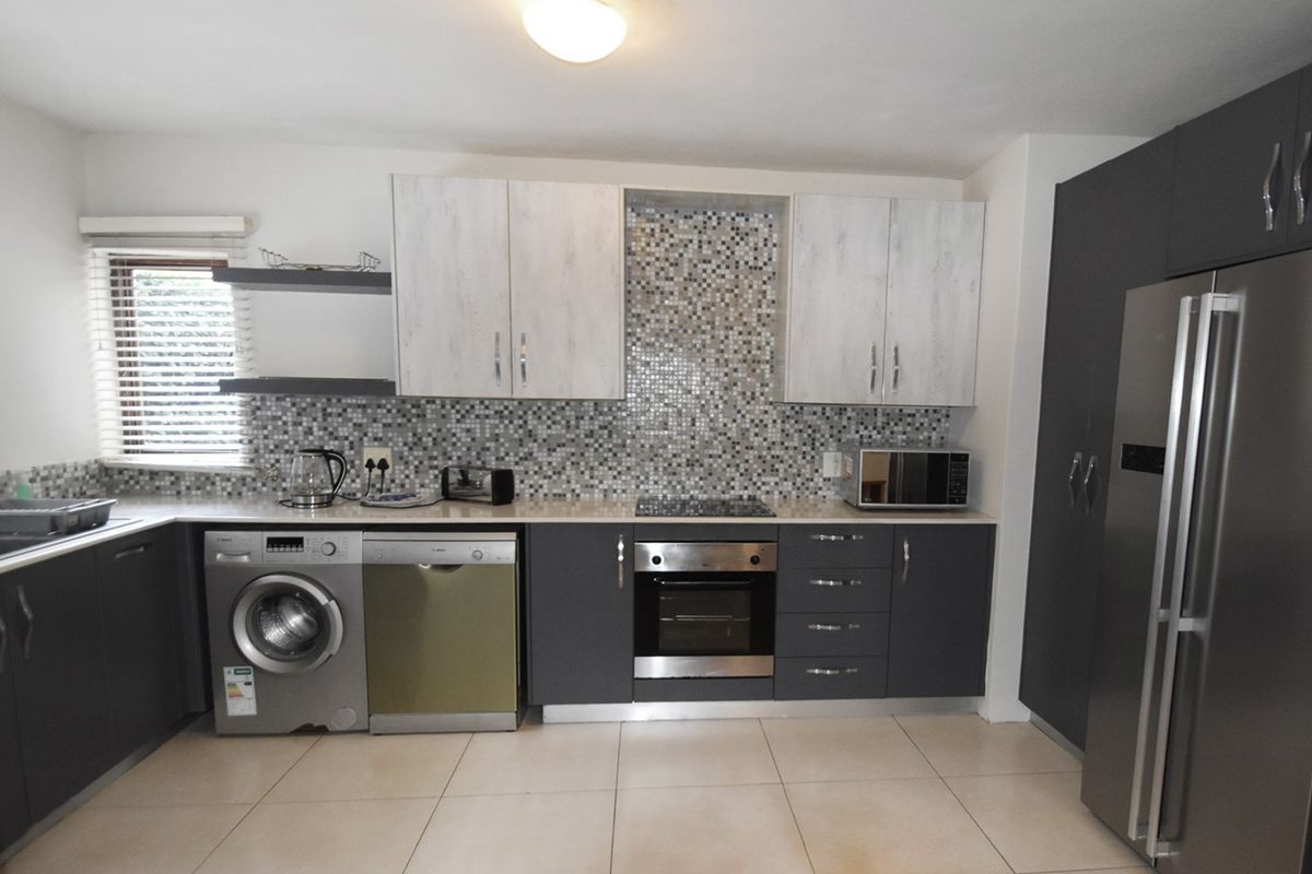 Modern kitchen featuring two-tone cabinetry, mosaic tile backsplash, integrated oven, hob, and tiled flooring with ample storage space.
