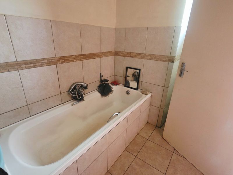 A functional bathroom featuring a built-in bathtub with ceramic wall and floor tiling, requiring some cosmetic updates to refresh the space.