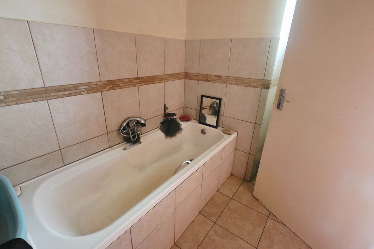 A functional bathroom featuring a built-in bathtub with ceramic wall and floor tiling, requiring some cosmetic updates to refresh the space.