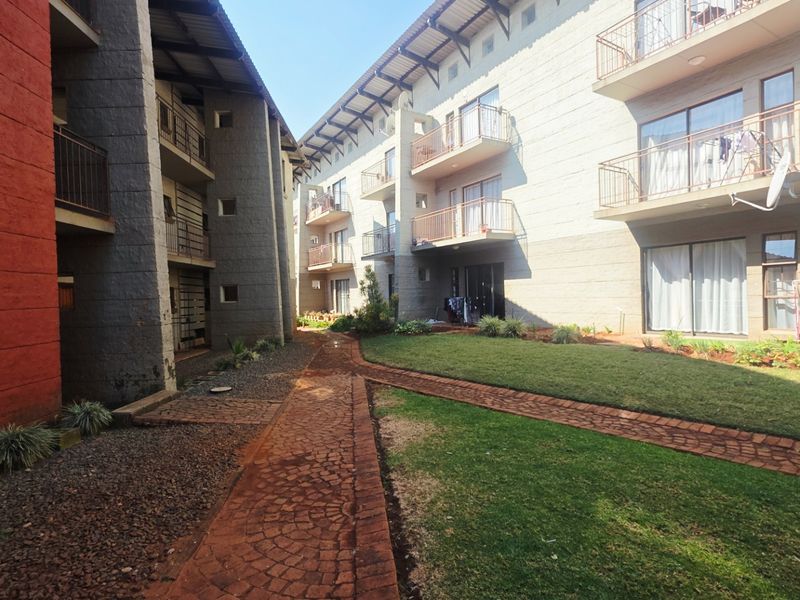 A view of the rear exterior of a multi-story residential complex featuring paved walkways, landscaped lawns, and private balconies.