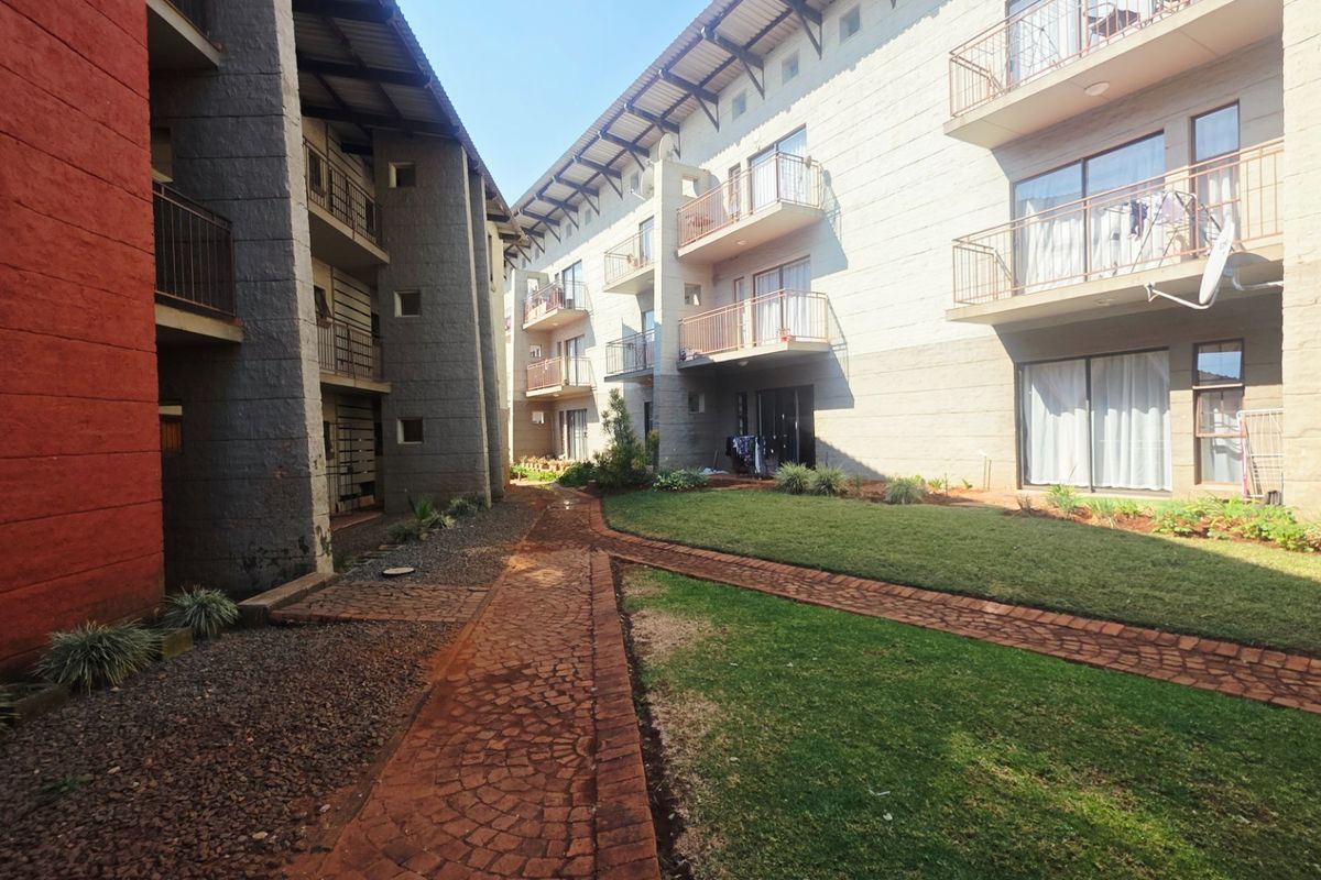 A view of the rear exterior of a multi-story residential complex featuring paved walkways, landscaped lawns, and private balconies.