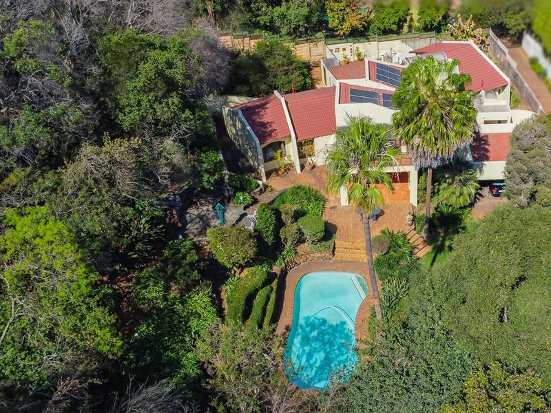 Aerial view of a residential property featuring a swimming pool, established garden, brick patio, and a tiled roof with solar panels.