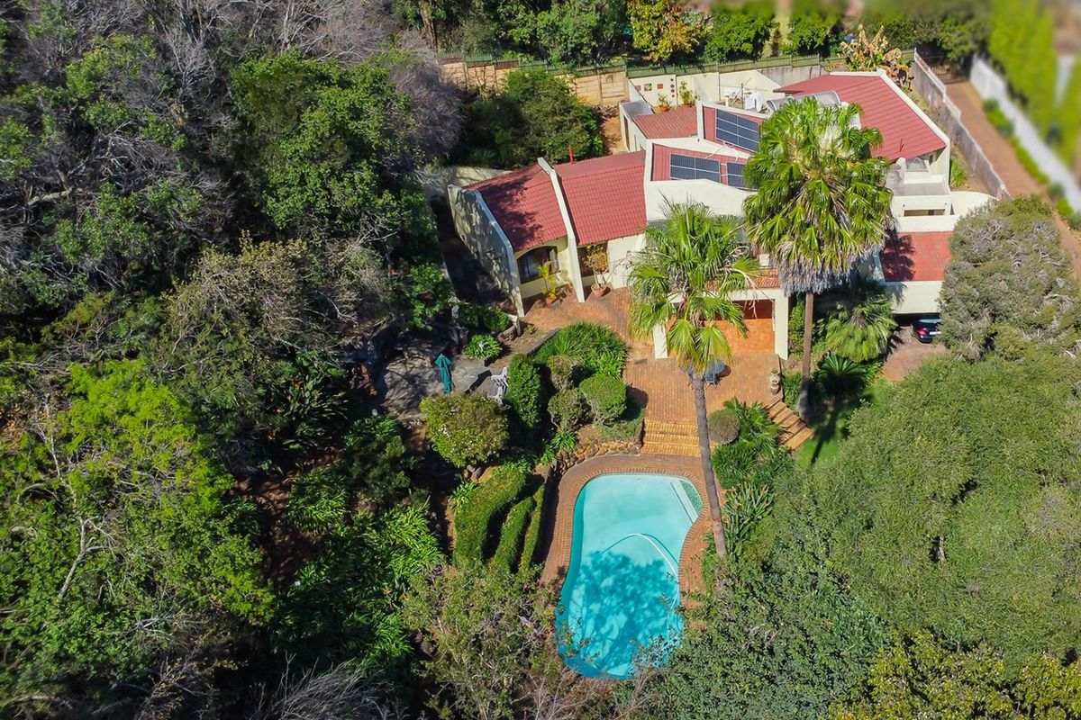 Aerial view of a residential property featuring a swimming pool, established garden, brick patio, and a tiled roof with solar panels.