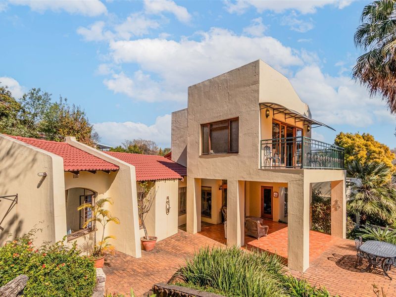 Rear view of a multi-level house featuring a covered ground floor patio, an upper-level balcony with metal railings, and terracotta roof tiles.