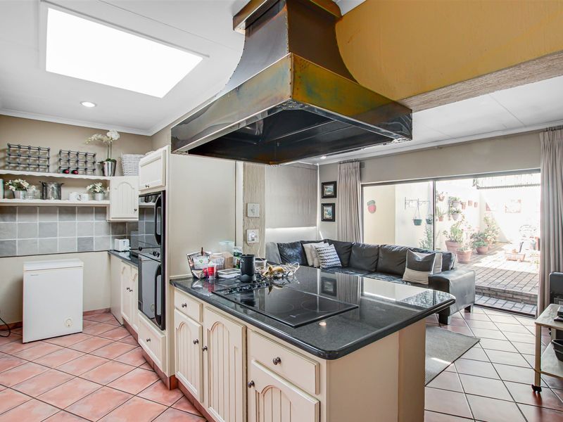 Open-plan kitchen and living area featuring a central island with granite countertops, built-in appliances, a large skylight, and direct access to an outdoor patio.