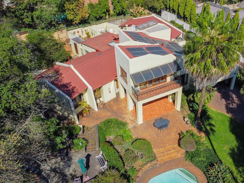 Aerial view of a residential property featuring a tiled roof with solar panels, a swimming pool, paved patio areas, and a landscaped garden.