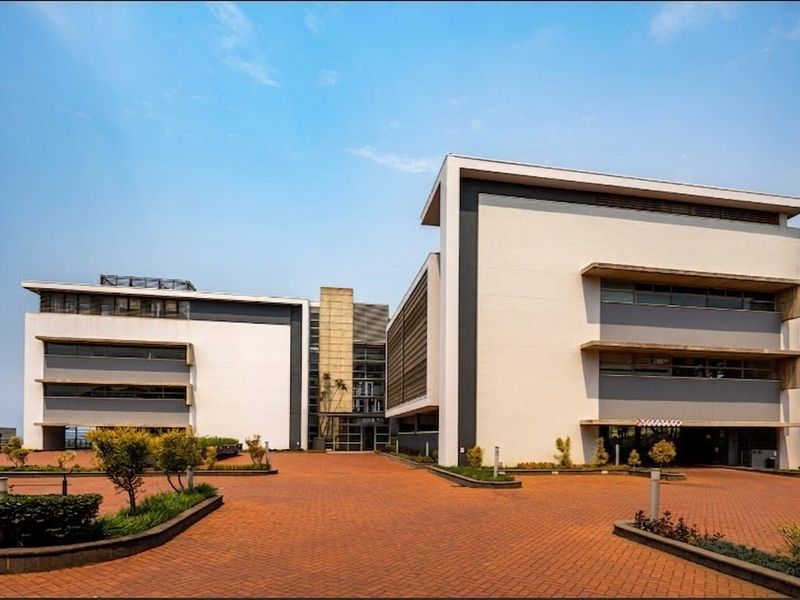 Modern multi-story office building featuring a paved driveway, clean architectural lines, and a prominent glass entrance facade.