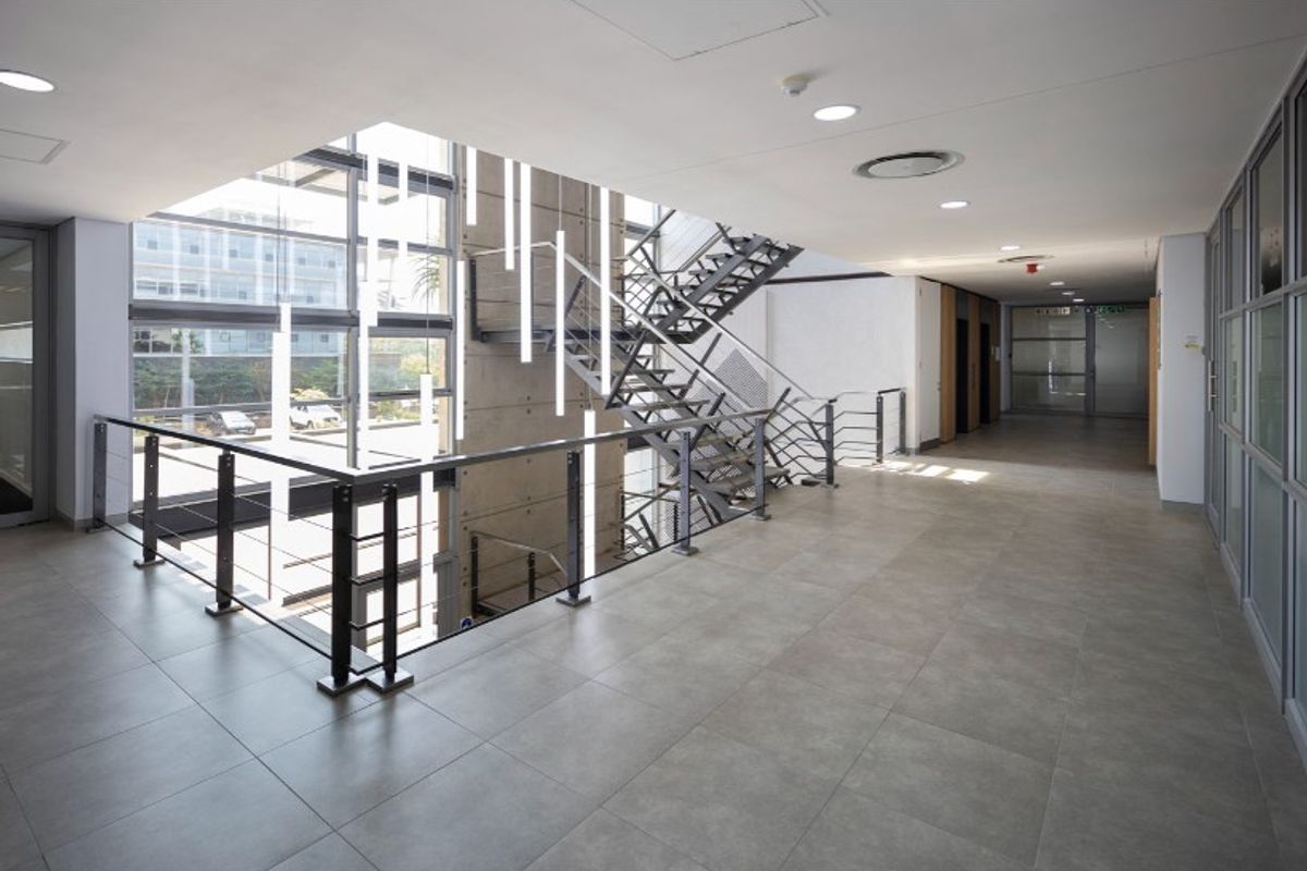 Modern office building hallway featuring a striking metal staircase, exposed concrete feature wall, and expansive glass curtain wall providing natural light.