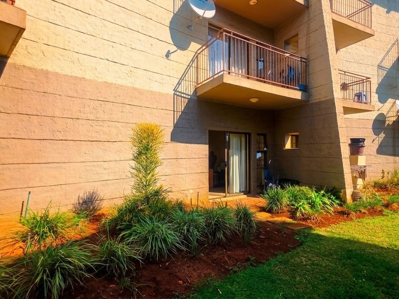 Rear view of the apartment building featuring private balconies with metal railings, sliding glass door access, and landscaped garden beds.