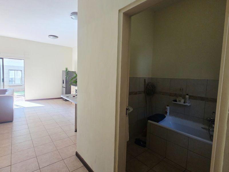 An open-plan living area with tiled flooring leading to a bathroom featuring a built-in bathtub and wall tiling.