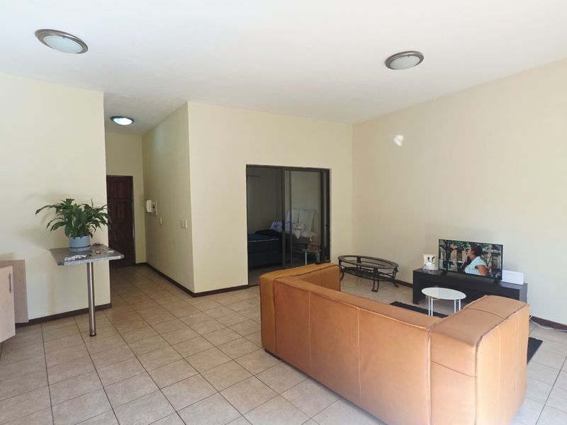 An open-plan living area featuring tiled flooring, neutral walls, and a compact kitchen section, providing a functional and versatile living space.