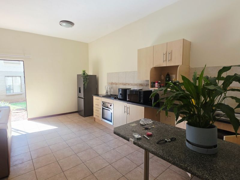 Open-plan living area featuring a functional kitchen with built-in cabinetry, granite countertops, and tiled flooring, leading out to an exterior patio area.