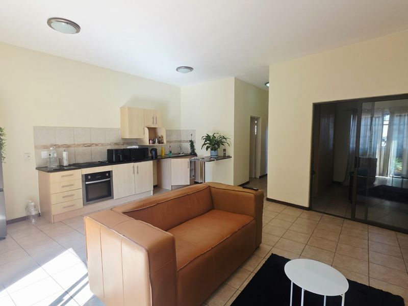 Open-plan living area featuring a functional kitchen with built-in cabinetry, oven, and hob, seamlessly connected to the living space with tiled flooring throughout.