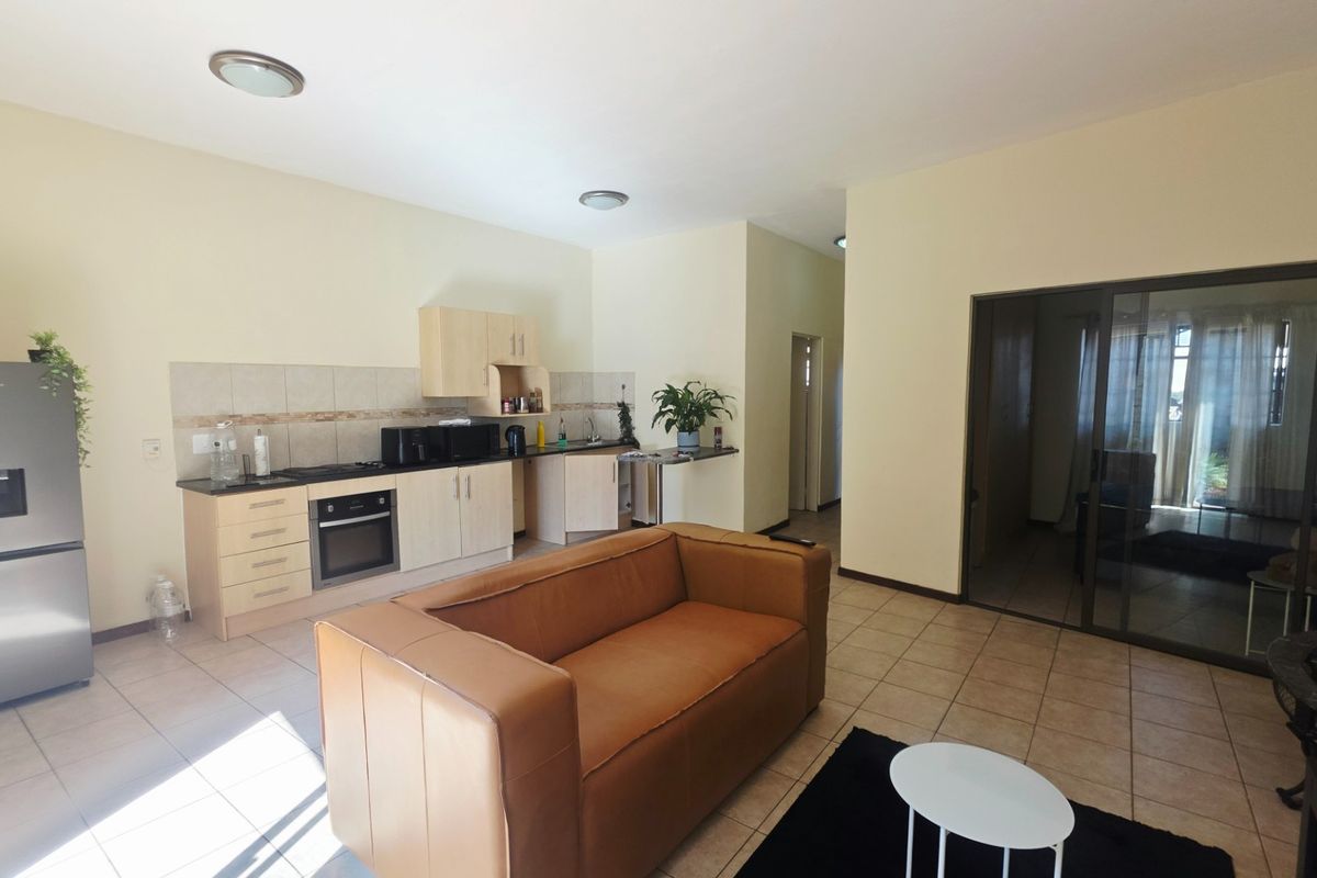 Open-plan living area featuring a functional kitchen with built-in cabinetry, oven, and hob, seamlessly connected to the living space with tiled flooring throughout.