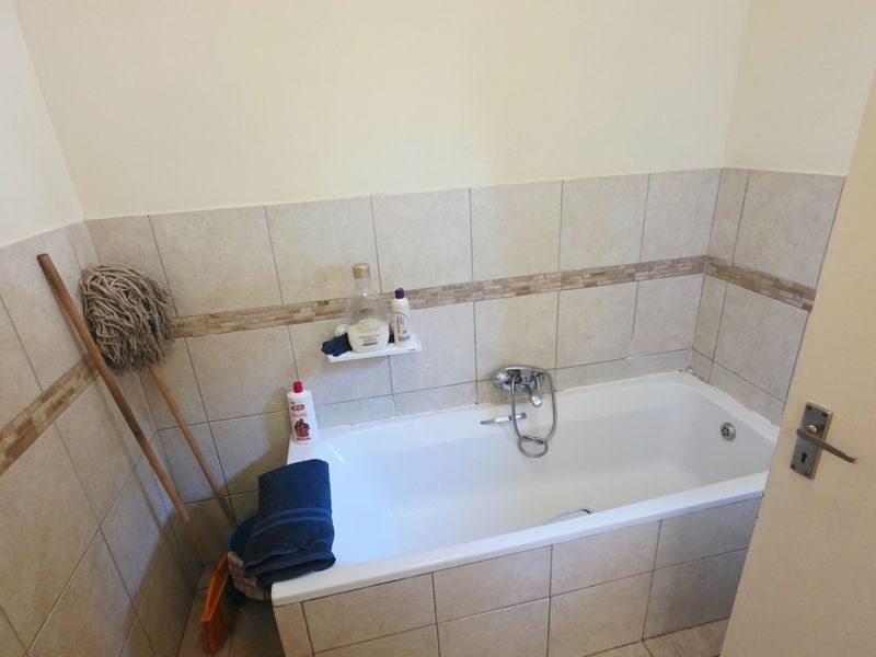 A functional bathroom featuring a standard bathtub with a mixer tap and neutral wall tiling.