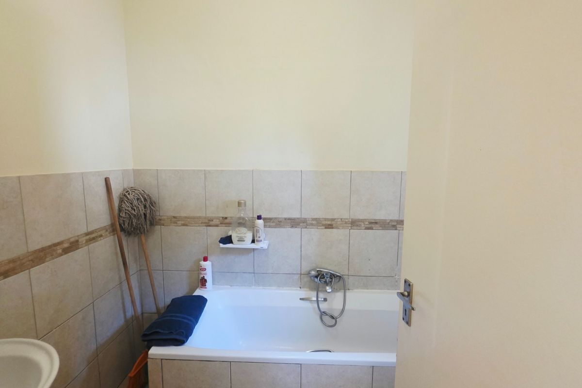 A functional bathroom featuring a bathtub with a mixer tap, tiled wall finishes, and a pedestal basin.