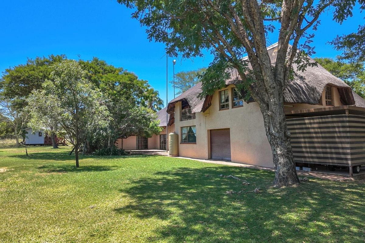 Rear view of a farm property featuring a traditional thatch roof, a roller shutter garage door, and a spacious garden area.