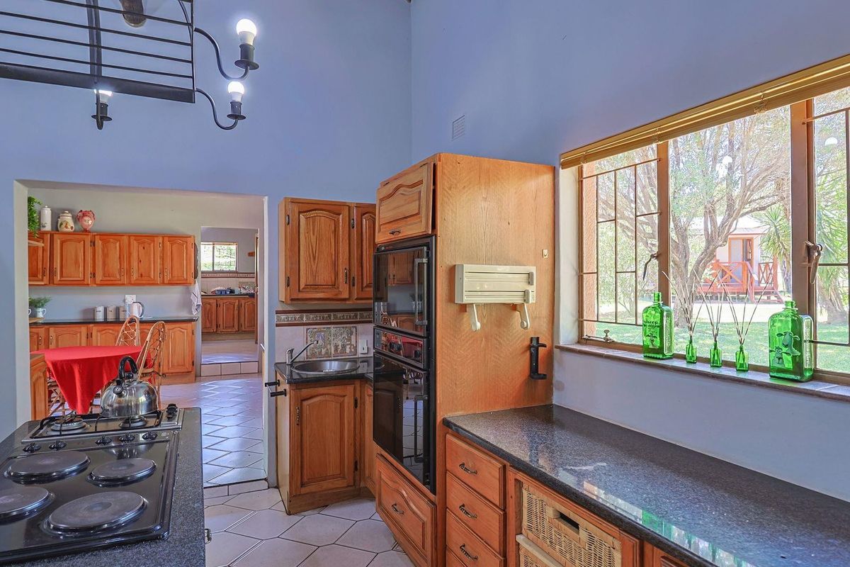 A traditional kitchen featuring wooden cabinetry, granite countertops, built-in oven, and electric hob, with an adjacent scullery area visible through the doorway.