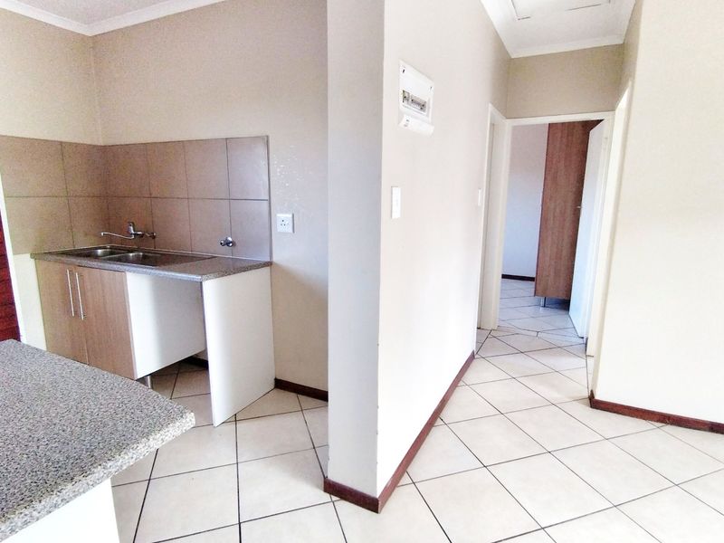 A functional kitchen area featuring built-in cabinetry, granite countertops, and a stainless steel sink, with tiled flooring extending into the adjacent hallway.