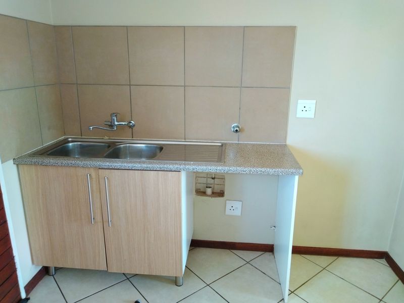 A compact kitchen area featuring a stainless steel sink, laminate countertop, tiled splashback, and base cabinetry with an open space for an appliance.