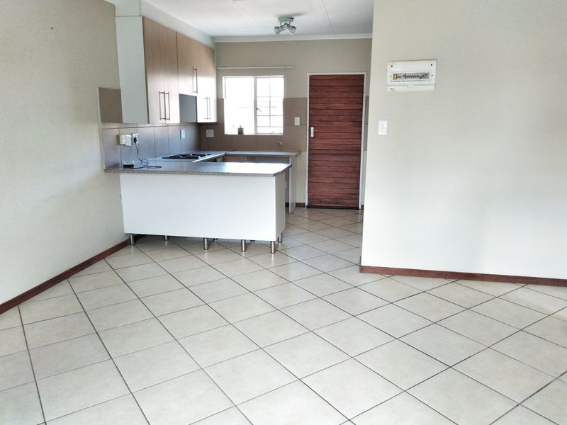 Open-plan living area featuring tiled flooring and a functional kitchen with built-in cabinetry, hob, and extractor fan.