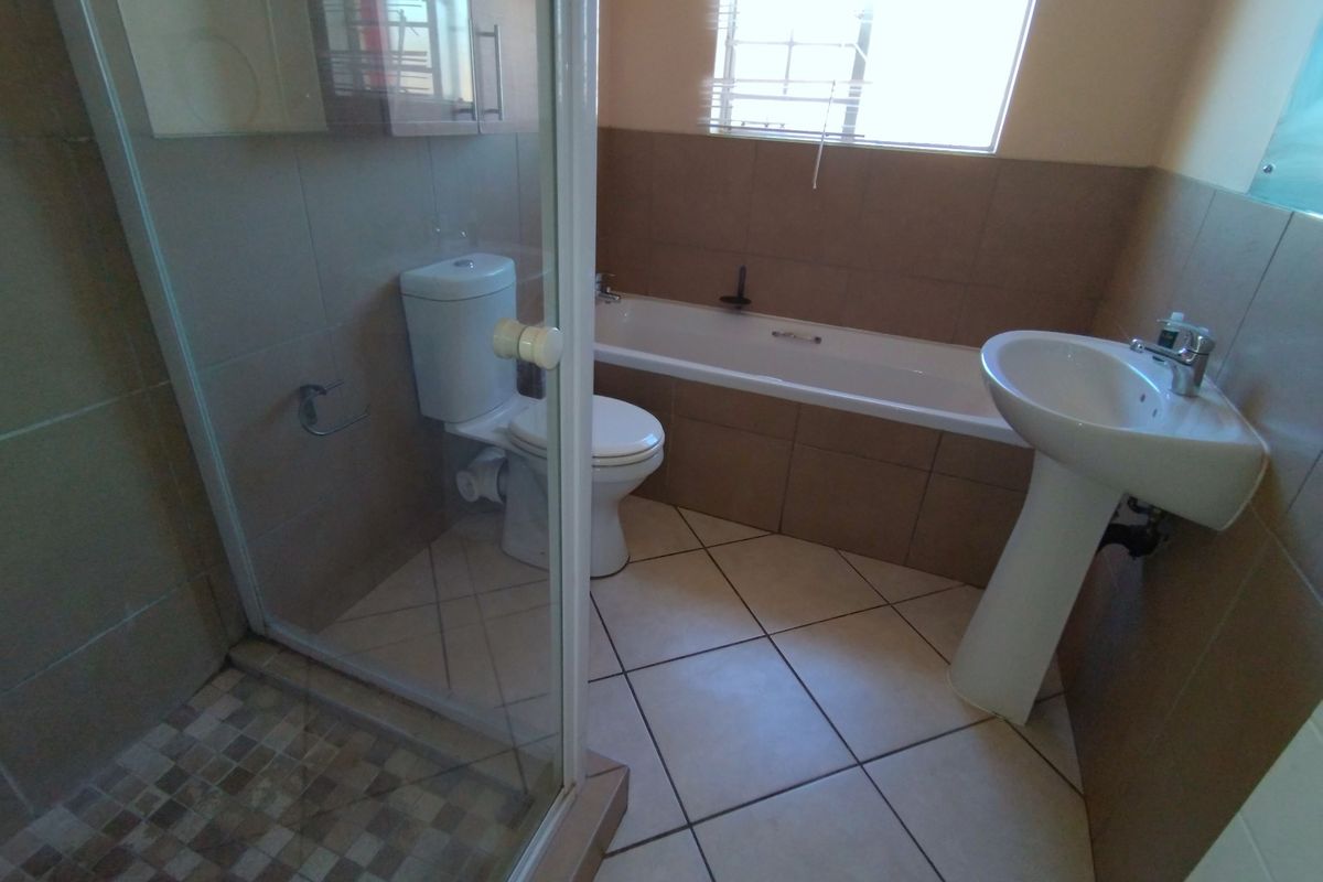 A functional bathroom featuring a pedestal basin, built-in bathtub, and a separate glass-enclosed shower with neutral wall and floor tiling.