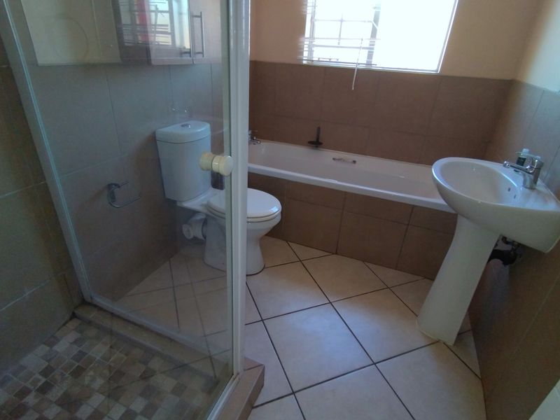 A functional bathroom featuring a pedestal basin, built-in bathtub, and a separate glass-enclosed shower with neutral wall and floor tiling.