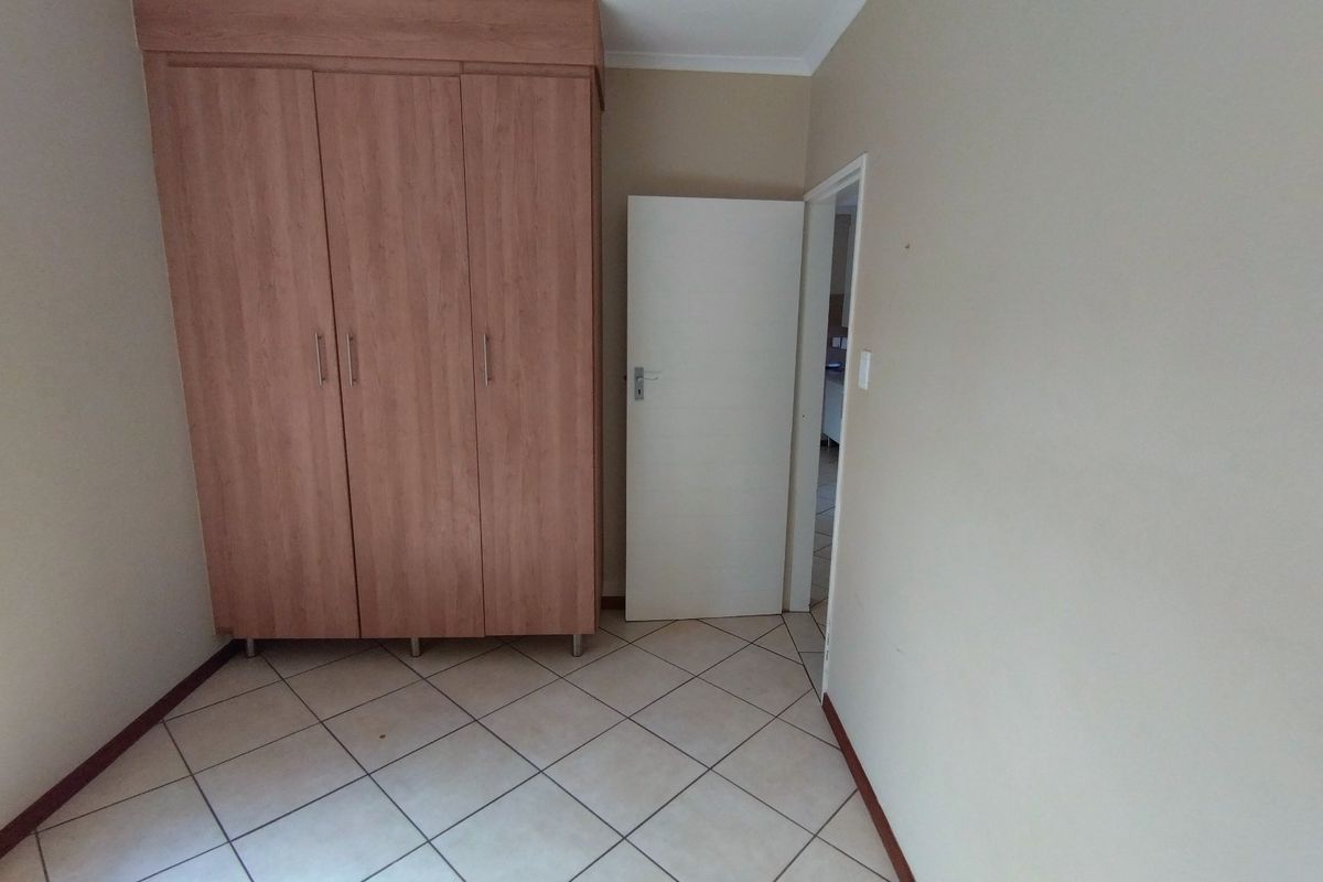 A simple bedroom featuring neutral tiled flooring and a built-in wooden wardrobe, offering a clean and functional space.