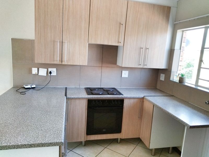 A clean, functional kitchen featuring light wood-finish cabinetry, granite-look laminate countertops, a built-in oven, and an electric hob with tiled backsplash.