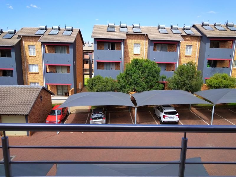 Elevated view overlooking the apartment complex courtyard, featuring paved parking areas with shade structures and buildings equipped with solar water heating systems.