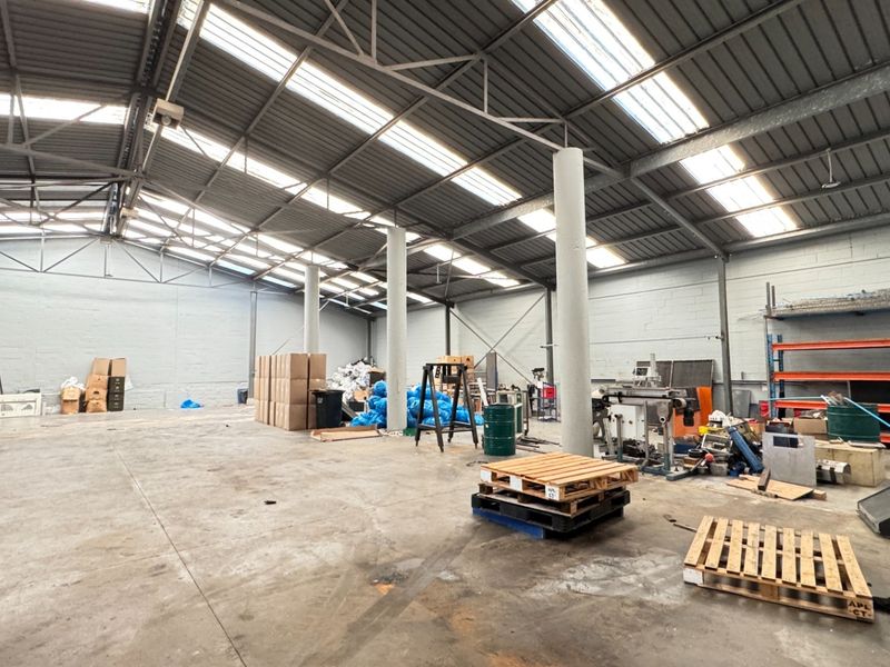 Spacious industrial warehouse unit featuring high ceilings with skylights, concrete flooring, and exposed structural steel elements, suitable for storage or manufacturing operations.
