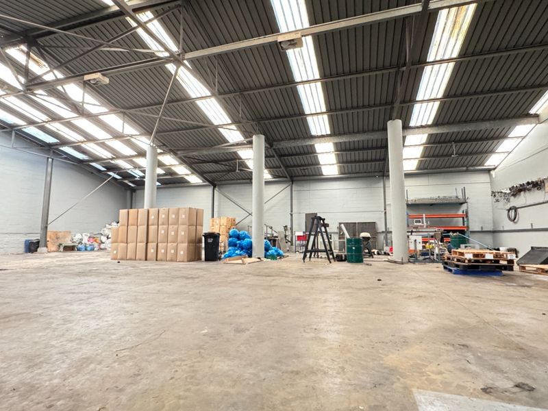 Spacious industrial warehouse unit featuring high ceilings with translucent roof panels, exposed steel trusses, and durable concrete flooring.