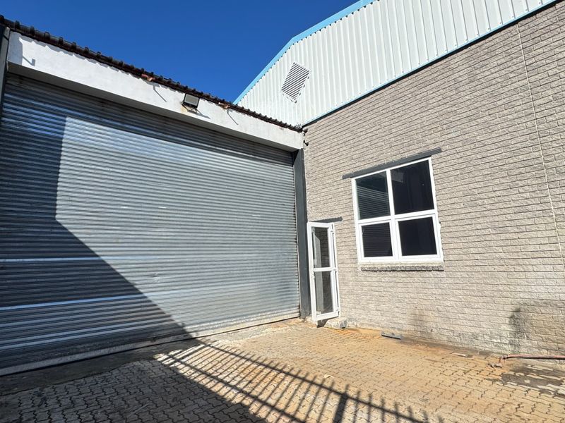 Rear exterior view of an industrial property featuring a large roller shutter door, brick facade, and paved yard area.