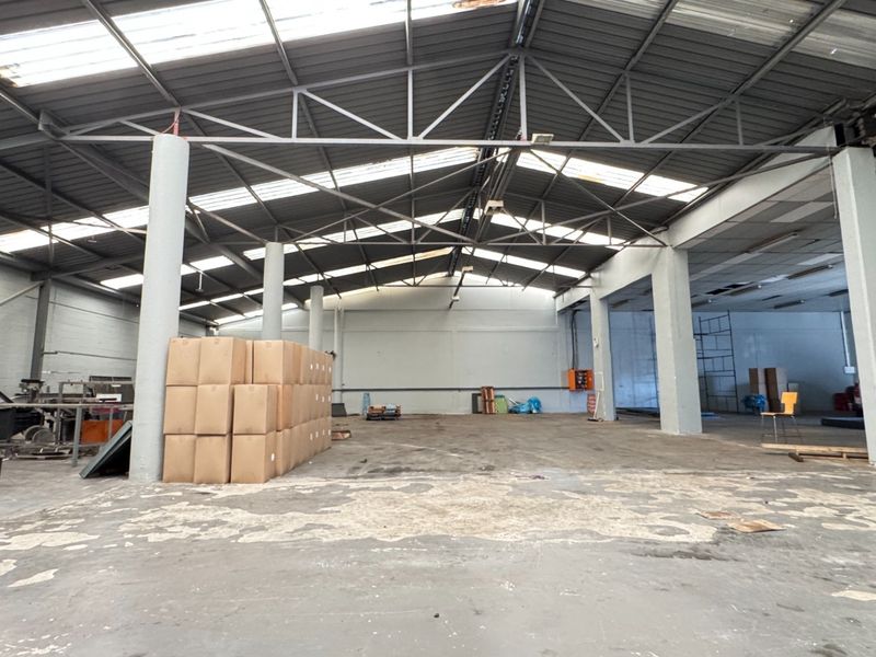 Spacious industrial warehouse featuring high exposed steel truss ceilings, natural light from skylights, concrete flooring, and structural support columns.