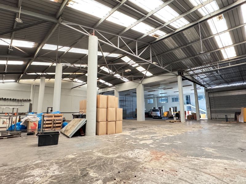 Spacious industrial warehouse featuring a high steel portal frame, translucent roof panels for natural light, concrete flooring, and a large roller shutter door.