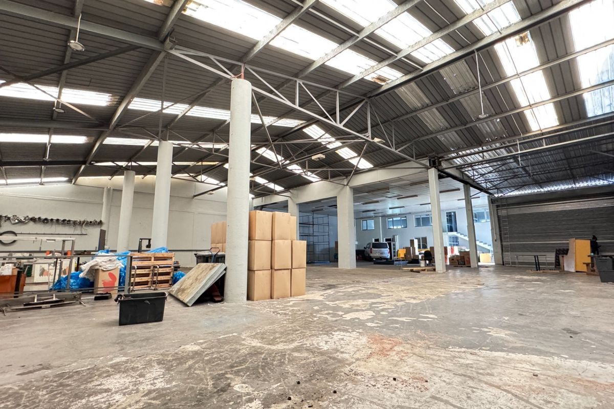 Spacious industrial warehouse featuring a high steel portal frame, translucent roof panels for natural light, concrete flooring, and a large roller shutter door.