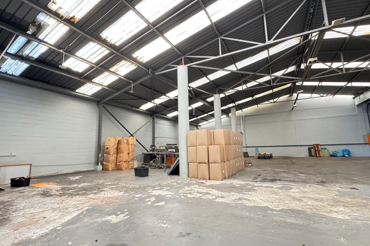 Spacious industrial warehouse unit featuring high steel truss ceilings with natural light panels and durable concrete flooring, suitable for storage or manufacturing operations.
