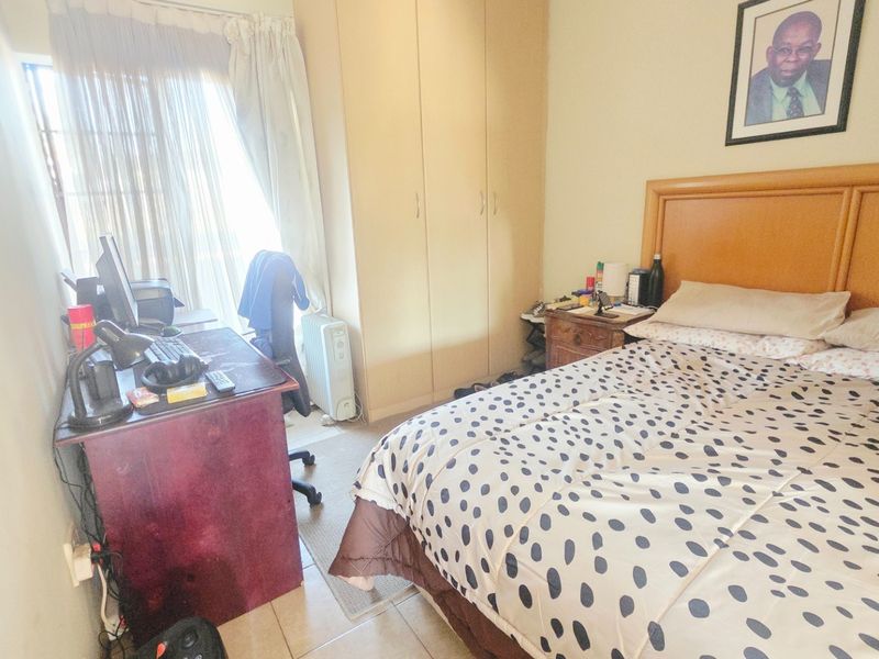 A functional bedroom featuring built-in cupboards and tiled flooring, offering a practical layout with natural light from the adjacent window.