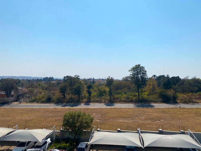 An elevated view overlooking a suburban landscape, featuring open fields, mature trees, and a parking area with shade-cloth carports.