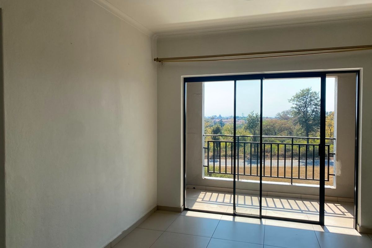 An empty bedroom featuring tiled flooring and a sliding glass door that opens onto a private balcony with scenic views.