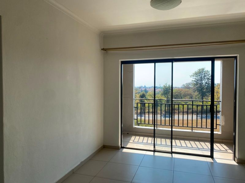 An empty bedroom featuring tiled flooring and a sliding glass door that opens onto a private balcony with scenic views.