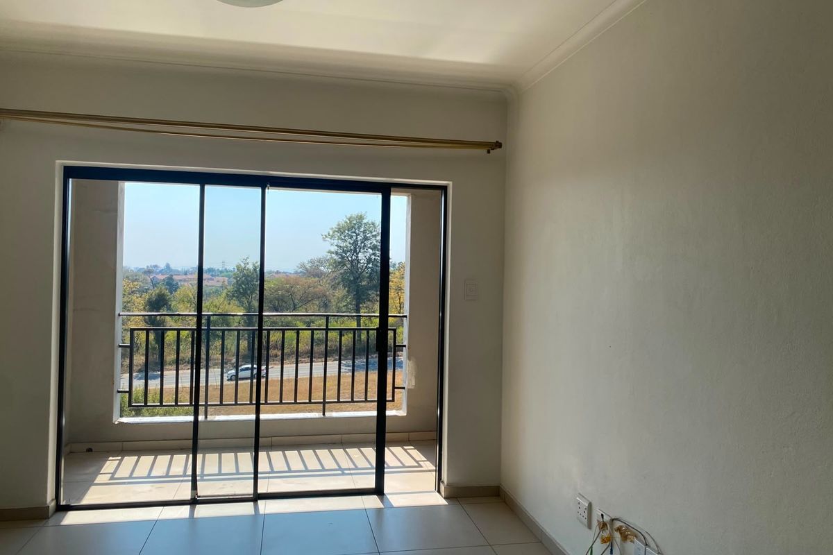 An empty living room featuring tiled floors and a sliding glass door that opens onto a balcony with scenic views.