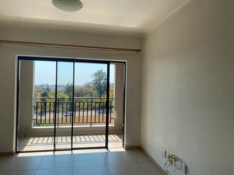 An empty living room featuring tiled floors and a sliding glass door that opens onto a balcony with scenic views.