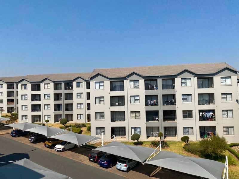 Exterior view of a multi-story apartment complex featuring tiled roofing, private balconies, and dedicated shade cloth parking bays for residents.