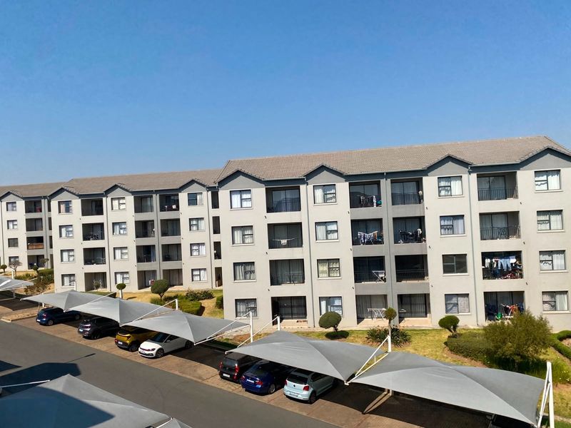 Exterior view of a multi-story apartment complex featuring a tiled roof, private balconies, and covered parking bays for residents.