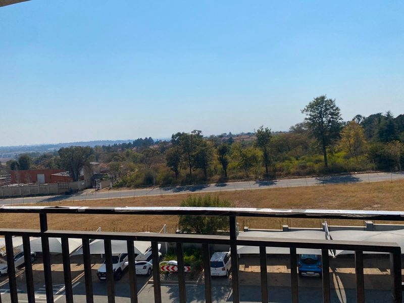 An elevated view from a balcony overlooking a parking area, open field, and surrounding landscape.