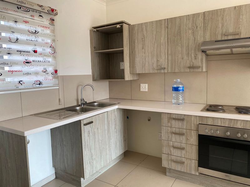 A functional kitchen featuring wood-look laminate cabinetry, built-in oven with hob, extractor fan, and a double stainless steel sink with tiled splashback.